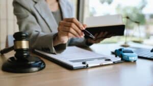 A lawyer signing a car contract with a gavel and a toy car on the desk, symbolizing car law, insurance, or legal agreement.