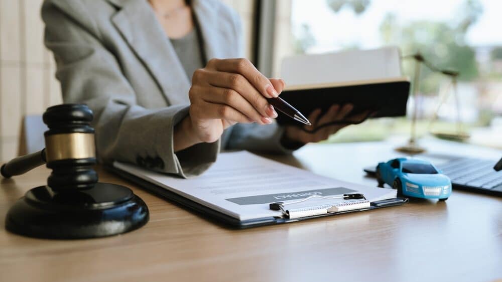 A lawyer signing a car contract with a gavel and a toy car on the desk, symbolizing car law, insurance, or legal agreement.
