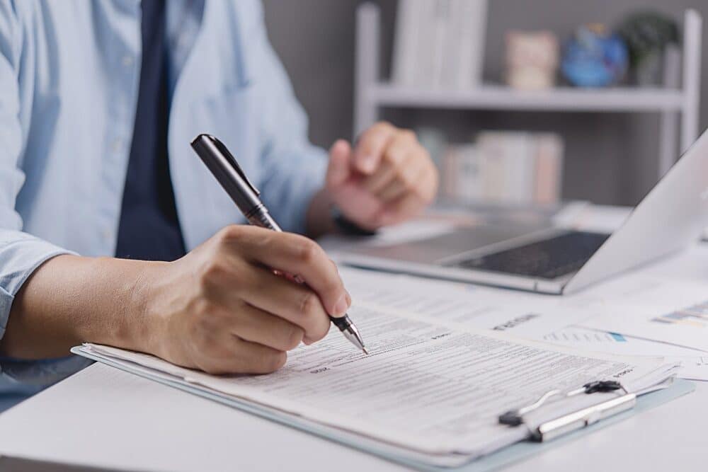 Businessman hand filling out tax return form or insurance application document