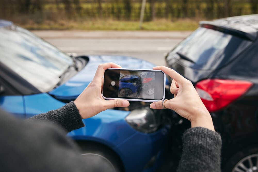 Close up of female driver taking photos of road traffic accident on mobile phone for insurance claim