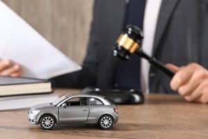 Auto accident law. Man with document and gavel at wooden table indoors, focus on toy car.