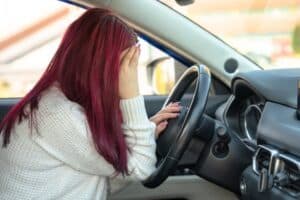 Woman behind the wheel of a car, holding her head: feeling unwell, accident