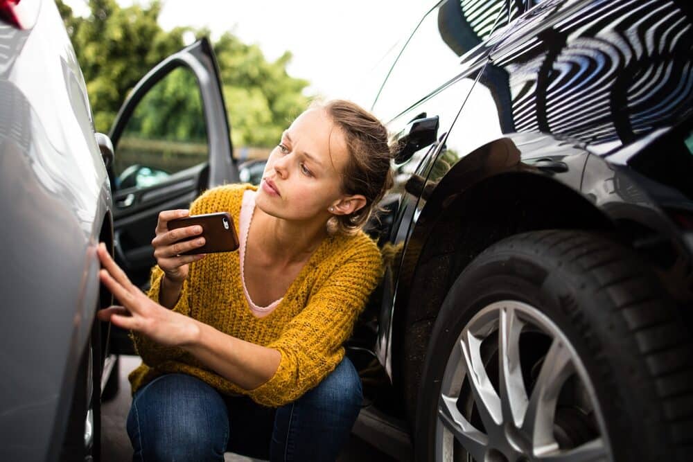 Pretty, young woman checking the state of a car for insurance purposes, prior to start driving it after renting it from a car rental.