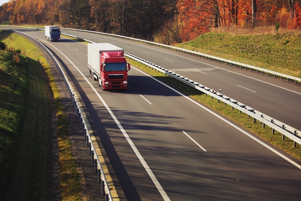 A truck with semi-truck drives through a wide landscape.