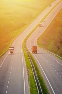 Trucks on the hilly highway road carrying goods in the sunlight