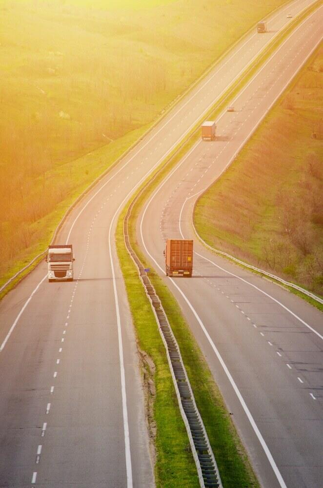 Trucks on the hilly highway road carrying goods in the sunlight