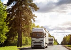 A column of trucks with semi-trailers transports cargo along a country road.