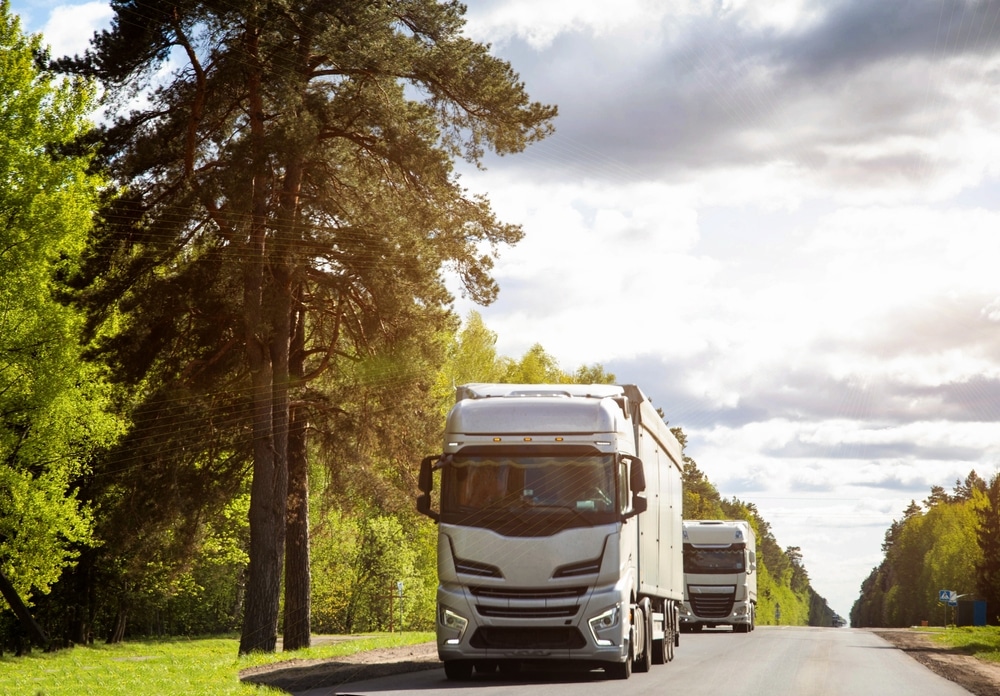 A column of trucks with semi-trailers transports cargo along a country road.