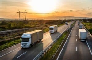 Highway transport. Transportation Trucks in lines passing on a rural countryside highway under a beautiful sunset sky.