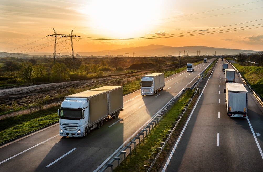 Highway transport. Transportation Trucks in lines passing on a rural countryside highway under a beautiful sunset sky.