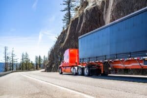 Industrial carrier long hauler red big rig semi truck tractor with extended cab for truck driver rest transporting cargo in dry van semi trailer driving on the winding mountain road in Columbia Gorge