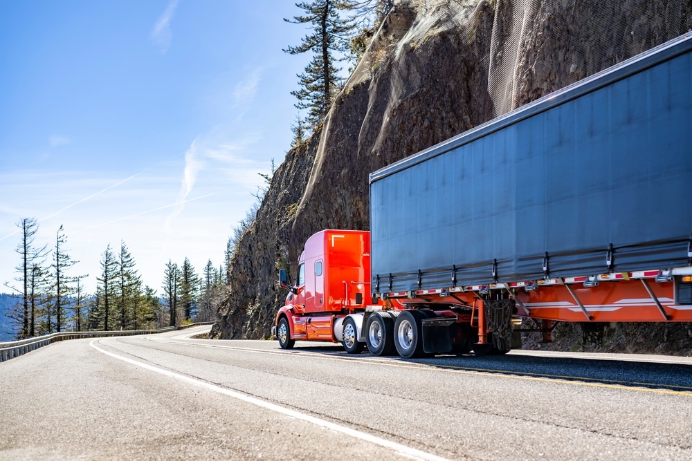 Industrial carrier long hauler red big rig semi truck tractor with extended cab for truck driver rest transporting cargo in dry van semi trailer driving on the winding mountain road in Columbia Gorge