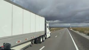 POV shot from a truck cabin showing a white semi-truck passing on the highway.