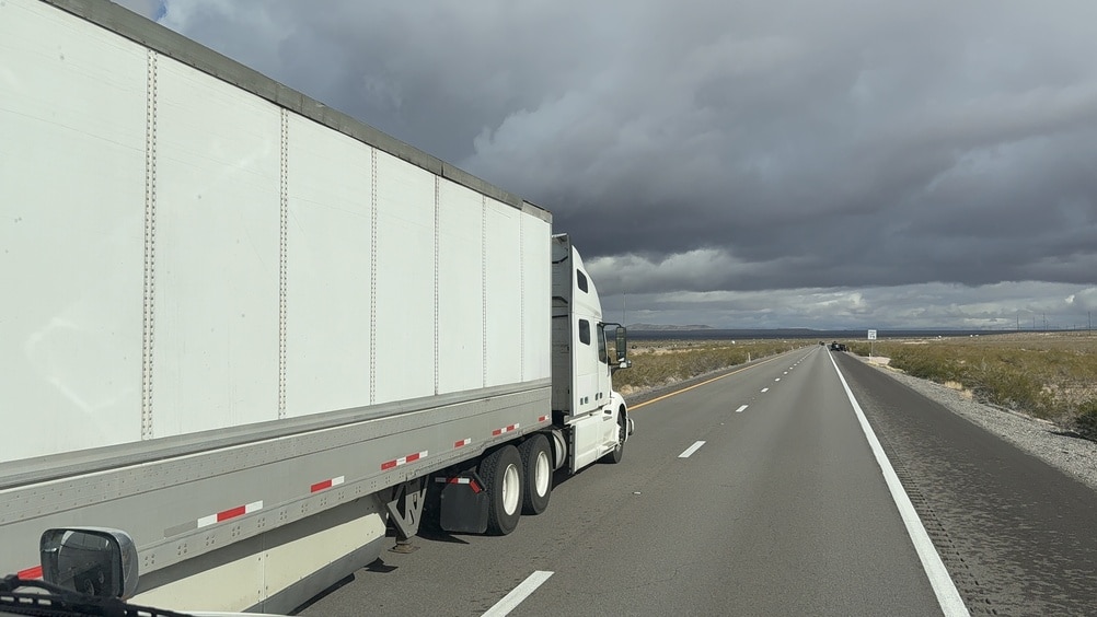 POV shot from a truck cabin showing a white semi-truck passing on the highway.