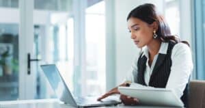 Office, serious and business woman on laptop for insurance, risk management or policy sales on internet.