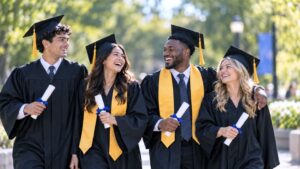 Four smiling college graduates in caps and gowns walking together on campus