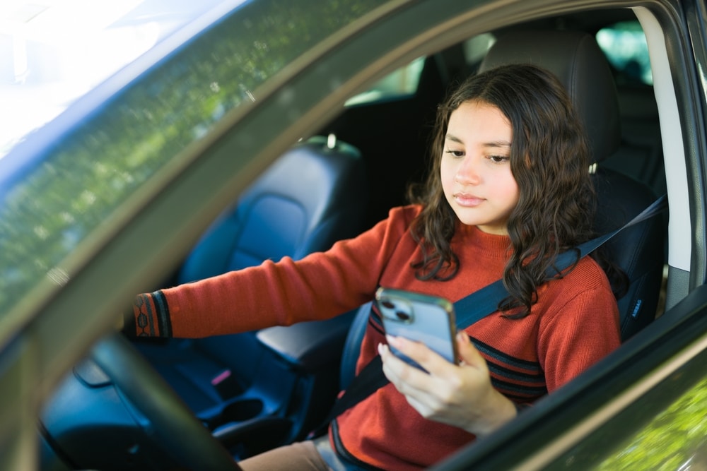 A woman looking at her phone while driving, showing one of the common instances of car accident negligence in California