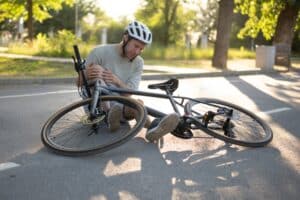 An injured bicyclist wearing a helmet sits on the road next to his bicycle after a crash, wondering how much compensation is available for a bicycle accident.