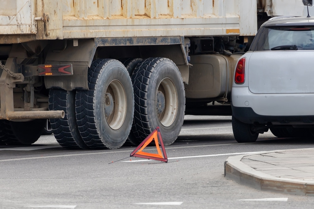 A truck and a car colliding on a city street, with a warning triangle in the foreground. Learn how to avoid truck accidents.