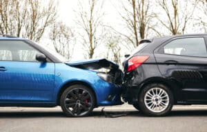 A car with a damaged hood sitting on the road behind another car. Find out who is at fault in a rear-end collision.