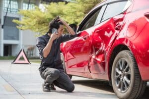 A man talking on the phone while kneeling next to a damaged car. Find out what diminished value claims are.