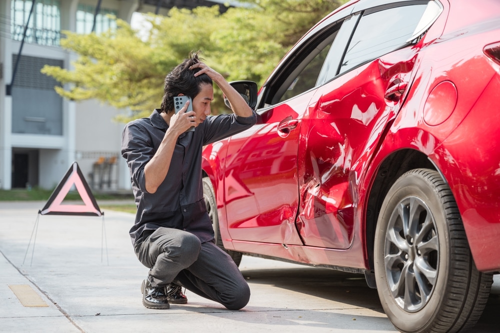 A man talking on the phone while kneeling next to a damaged car. Find out what diminished value claims are.